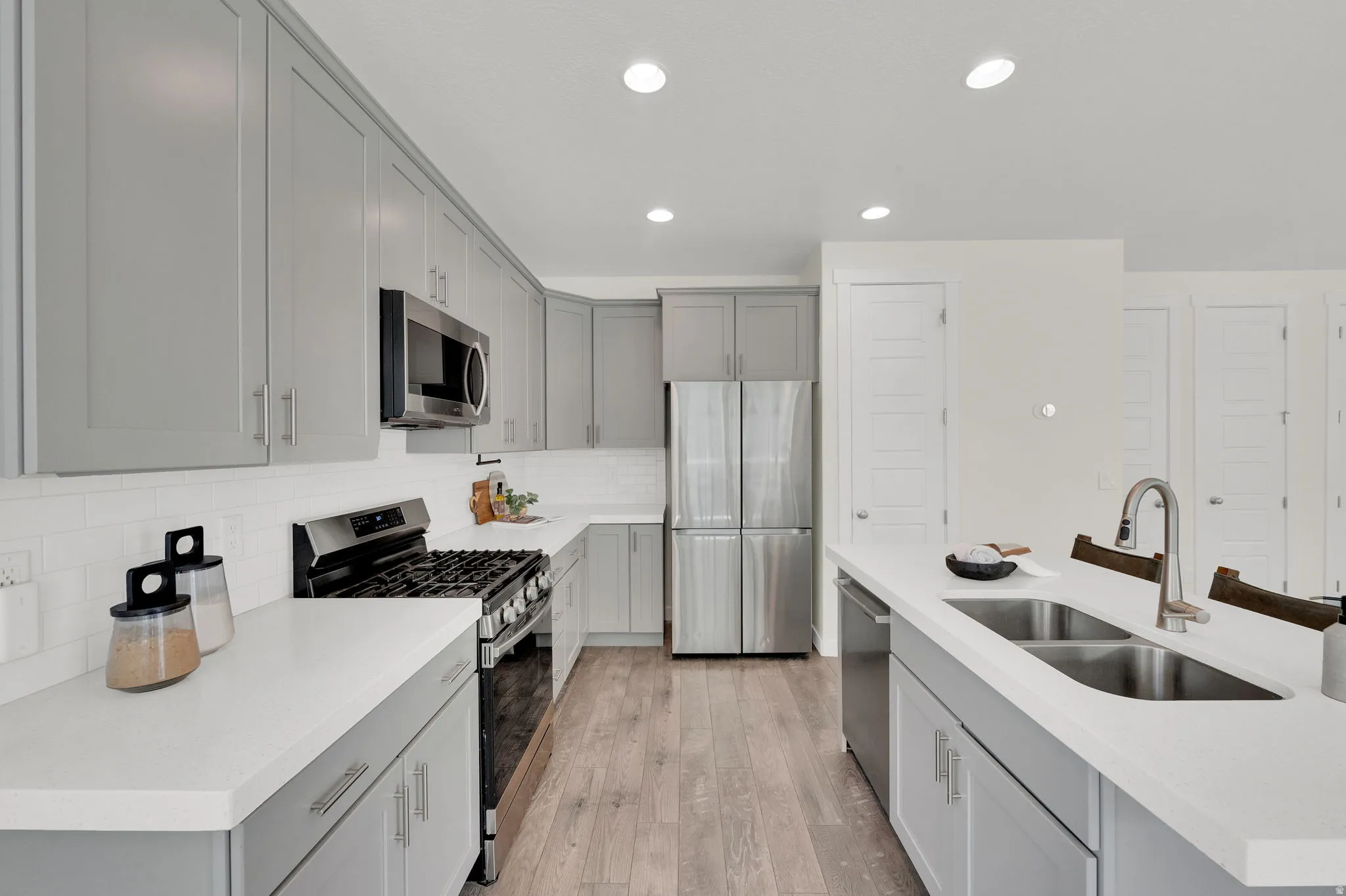 Kitchen featuring stainless steel appliances, gray cabinetry, light wood-style flooring, decorative backsplash, and light stone counters