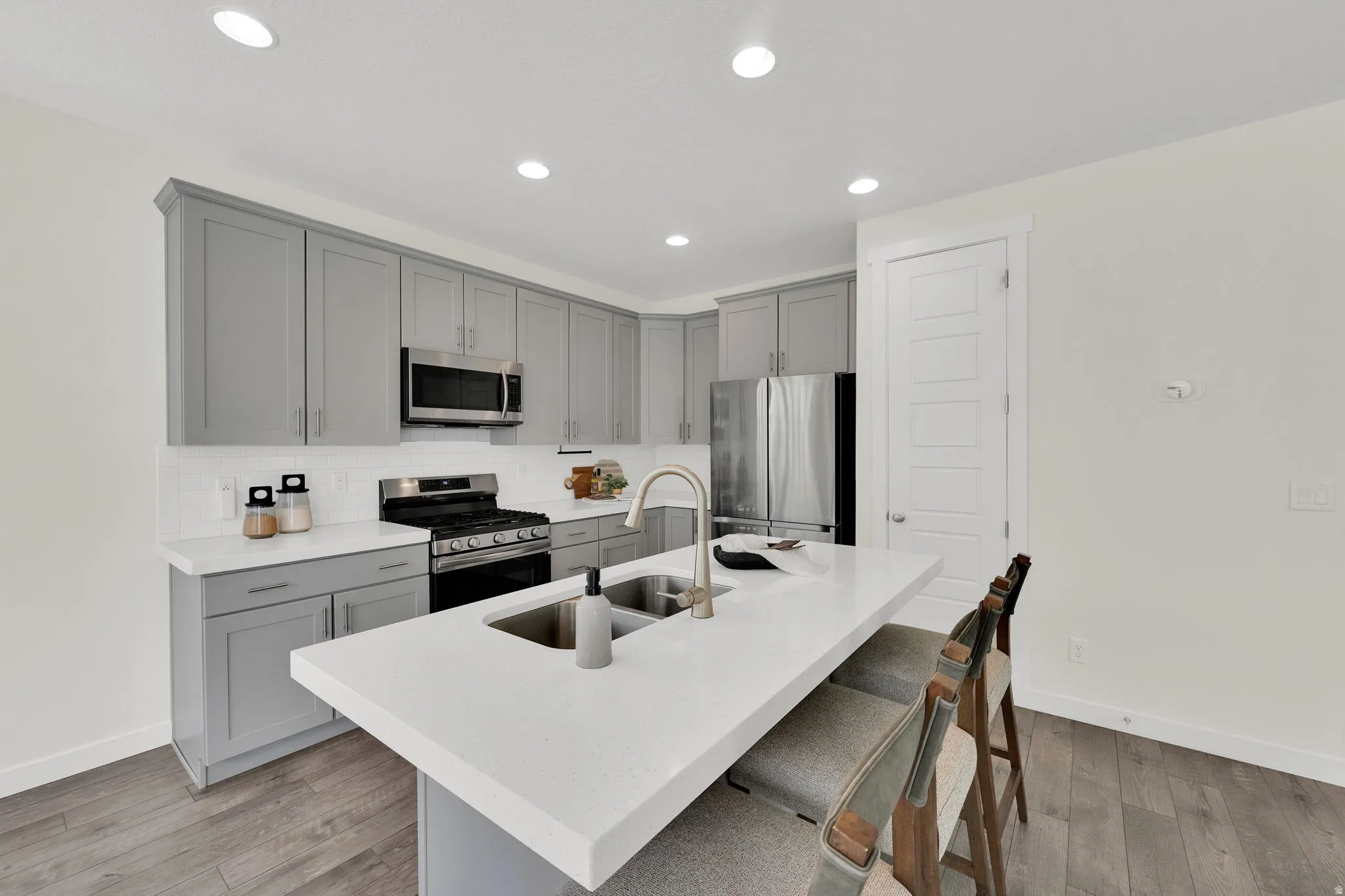 Kitchen featuring gray cabinets, stainless steel appliances, a kitchen bar, light wood-type flooring, and an island with sink