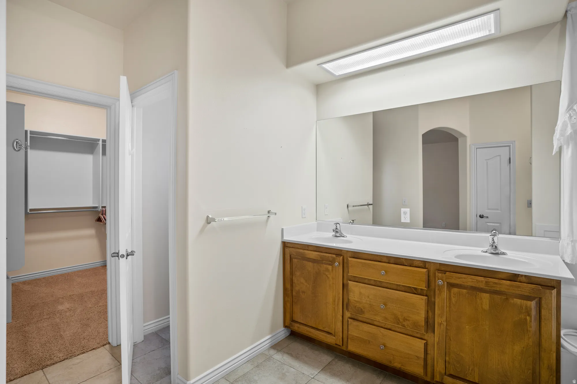 Full bath with double vanity, light tile patterned flooring, and a spacious closet