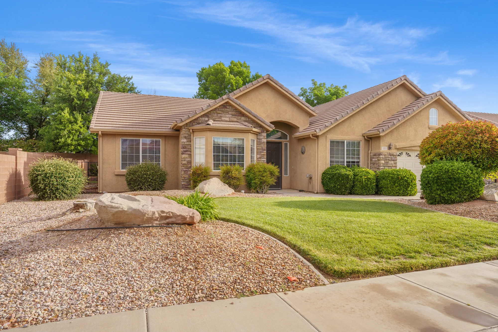 Single story home with stone siding, stucco siding, a garage, and a tile roof
