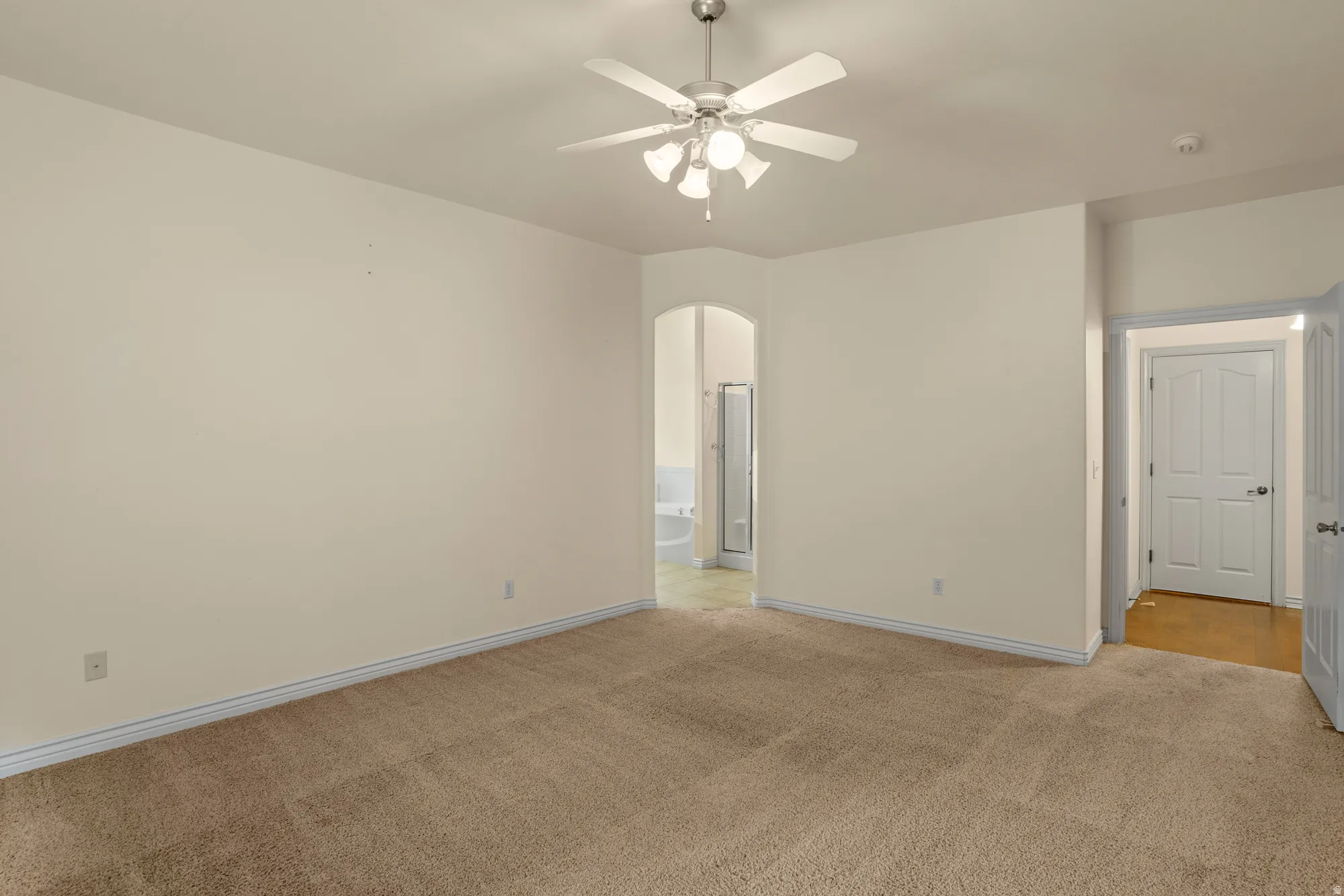 Unfurnished room with arched walkways, light colored carpet, and a ceiling fan