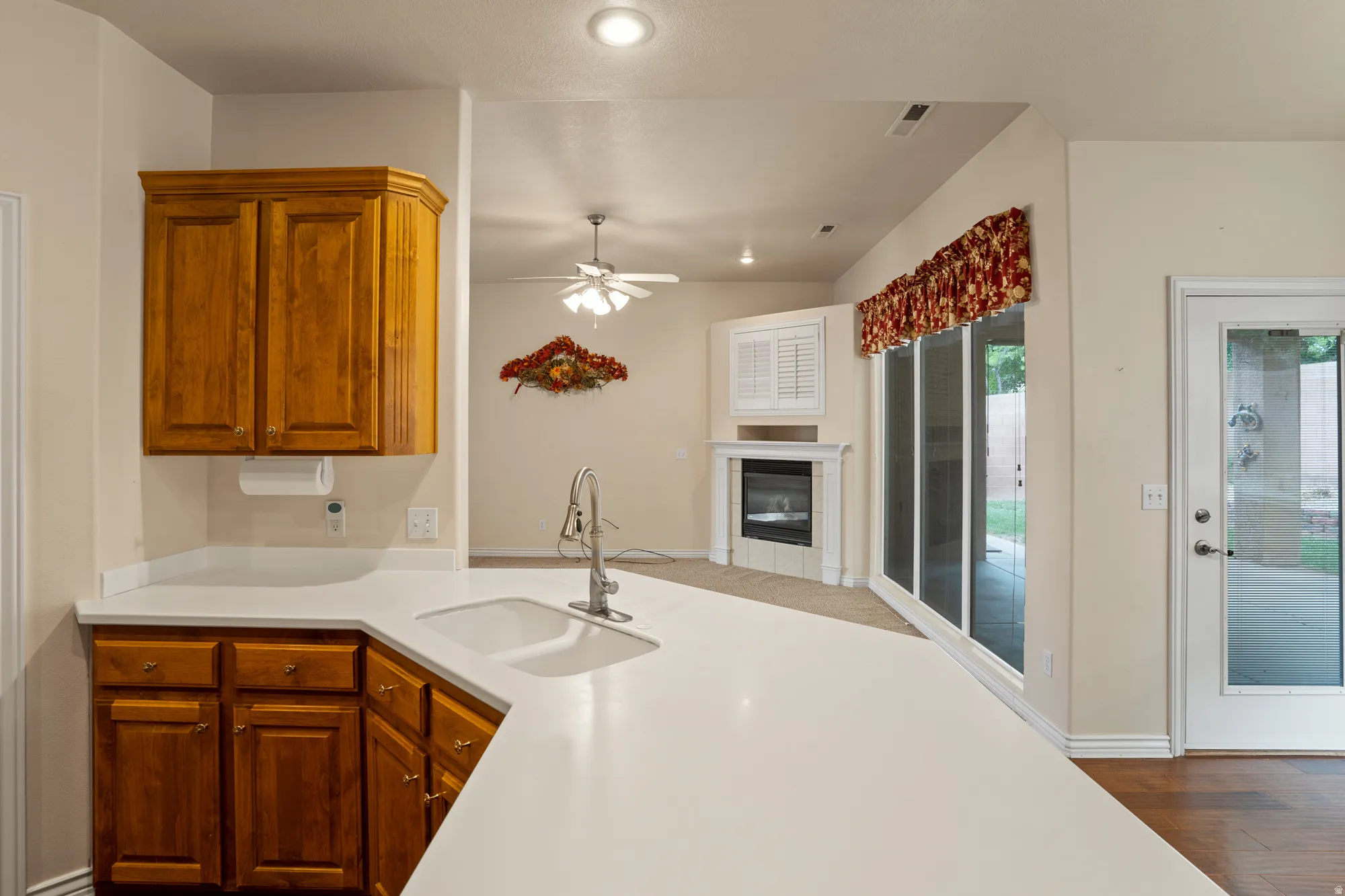 Kitchen with a tiled fireplace, wood finish cabinets, a ceiling fan, open floor plan, and dark wood-style flooring