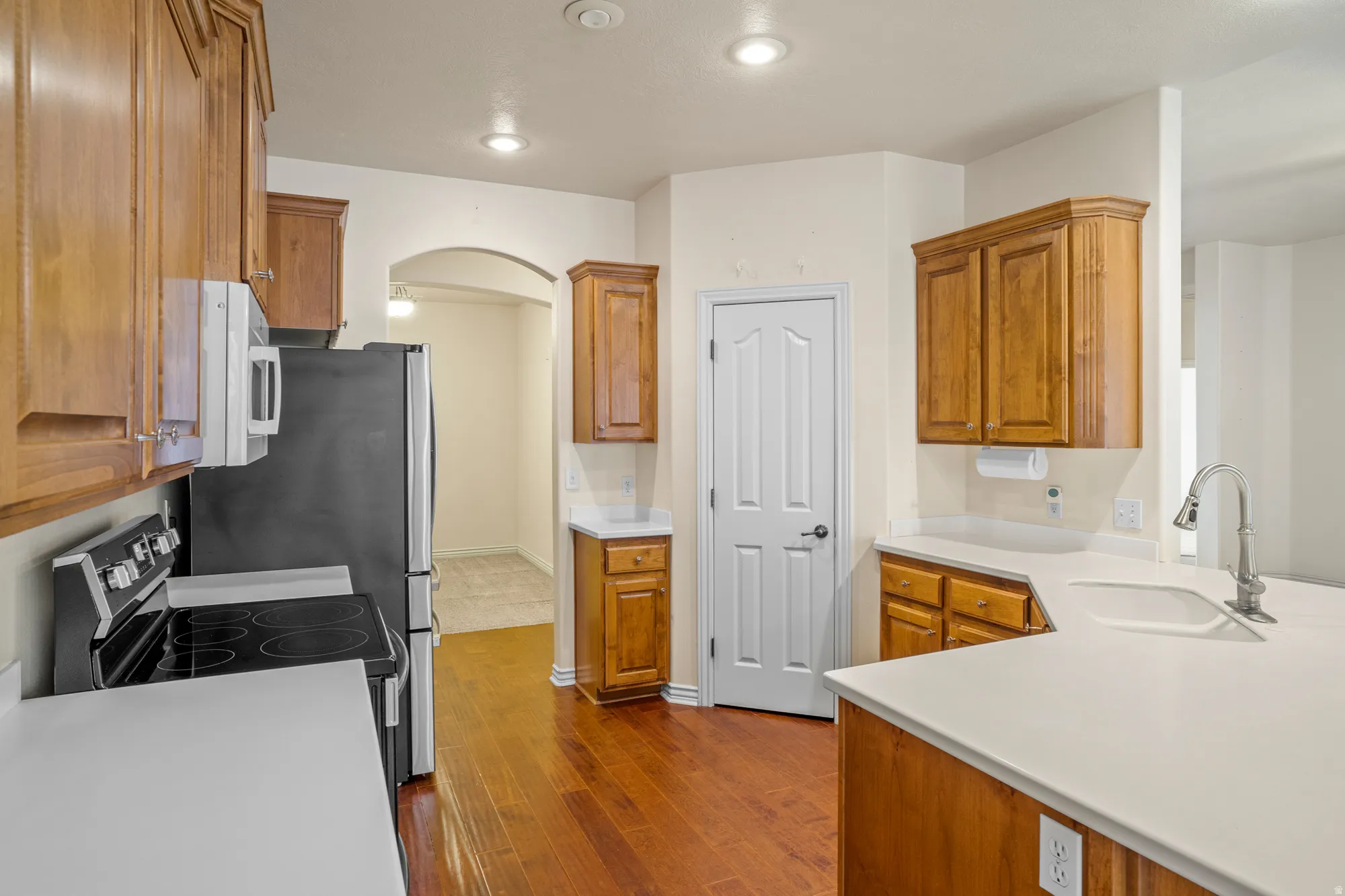 Kitchen featuring wood finish cabinetry, arched walkways, light countertops, stainless steel electric range oven, and dark wood-style floors