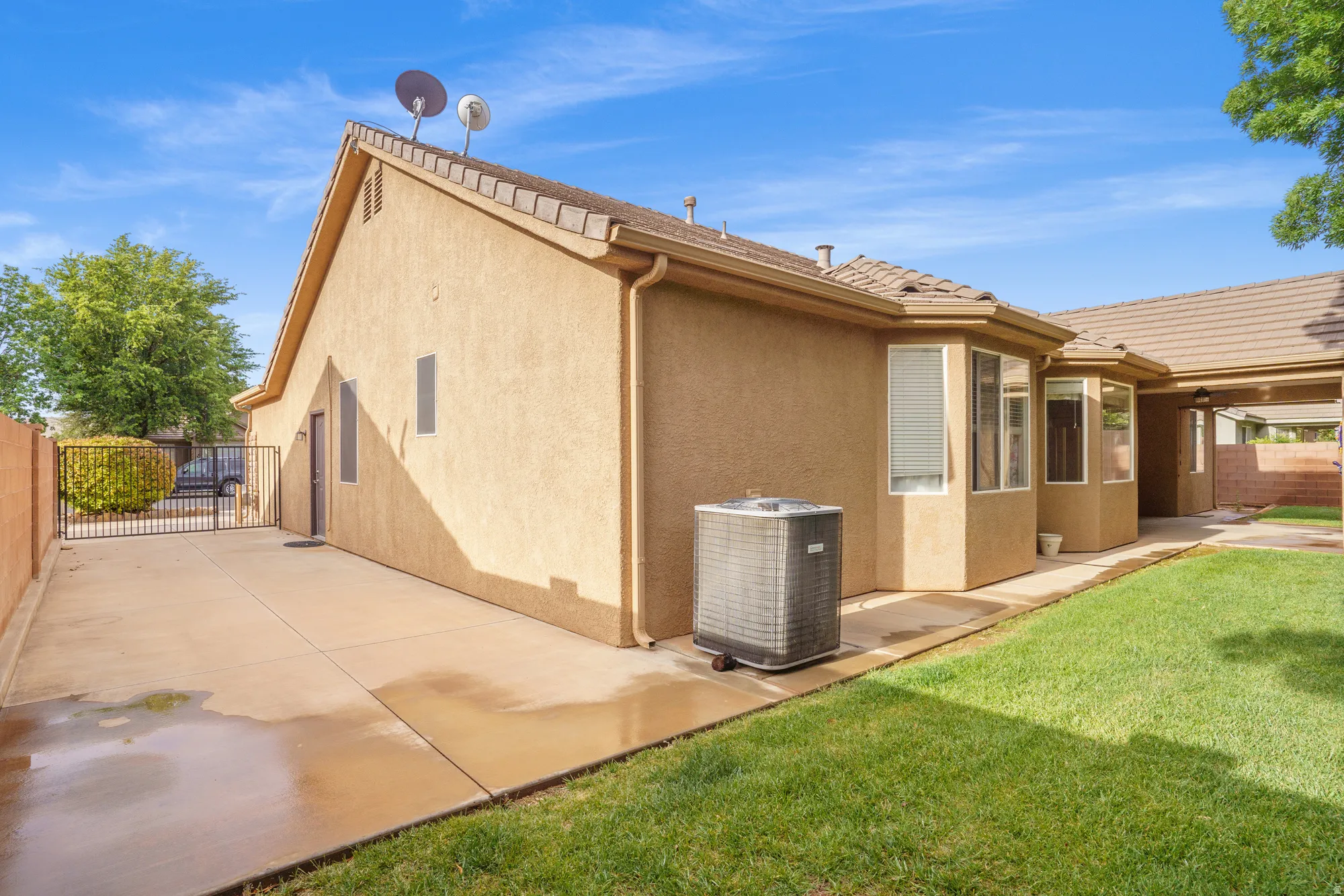 View of side of home featuring stucco siding, a fenced backyard, and a gate