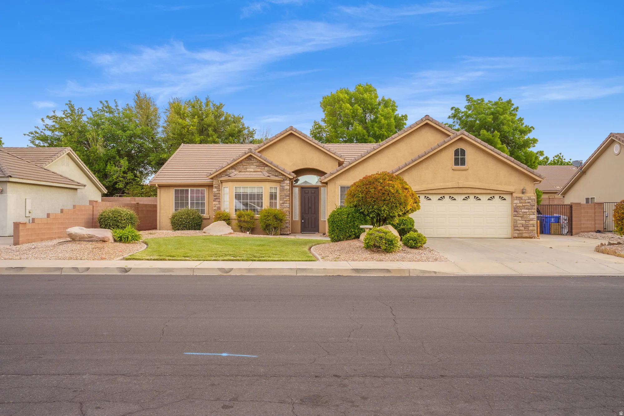Single story home with an attached garage, a tiled roof, stucco siding, driveway, and stone siding