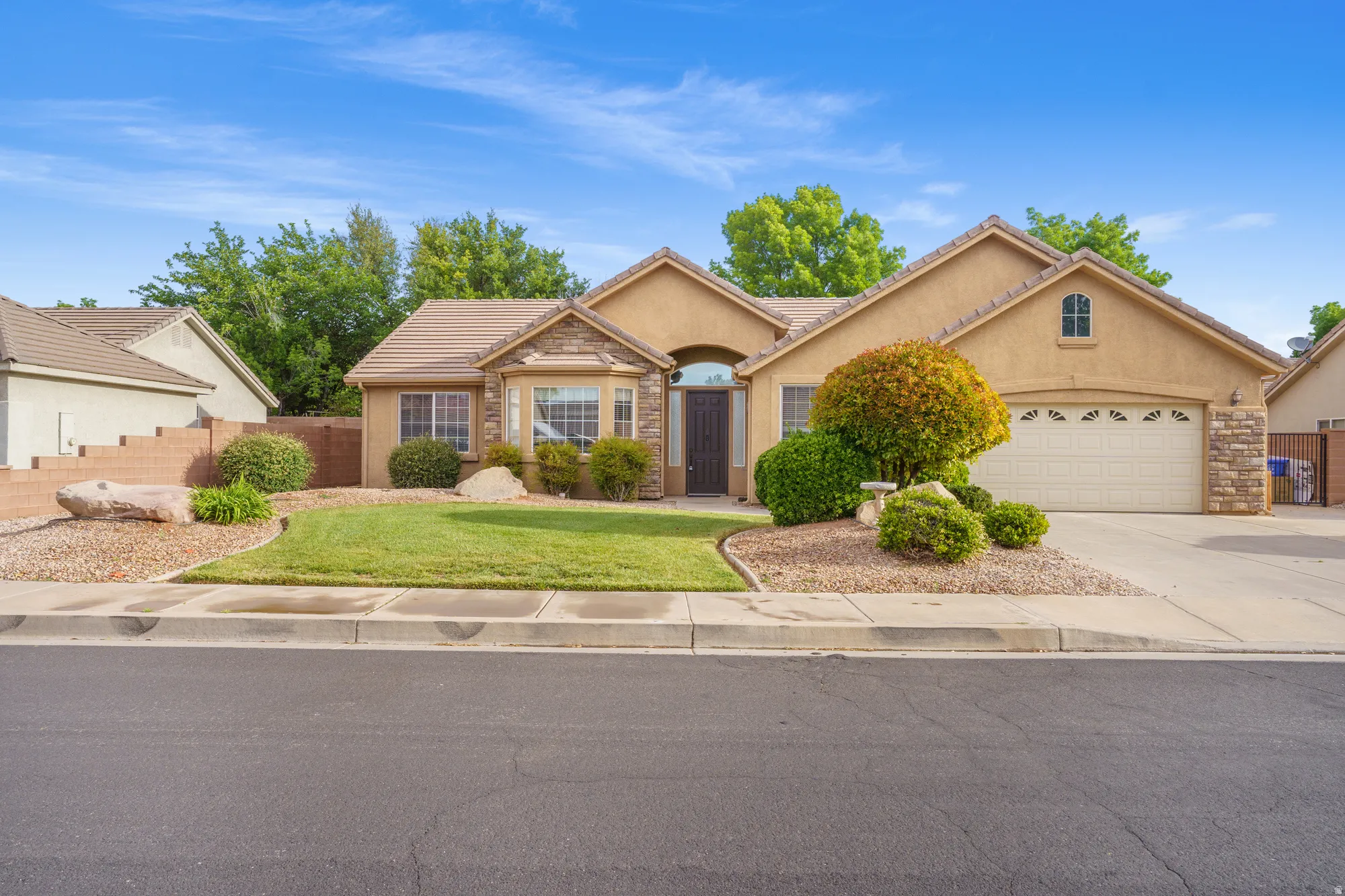 View of front of home with a garage, stucco siding, a tiled roof, concrete driveway, and stone siding