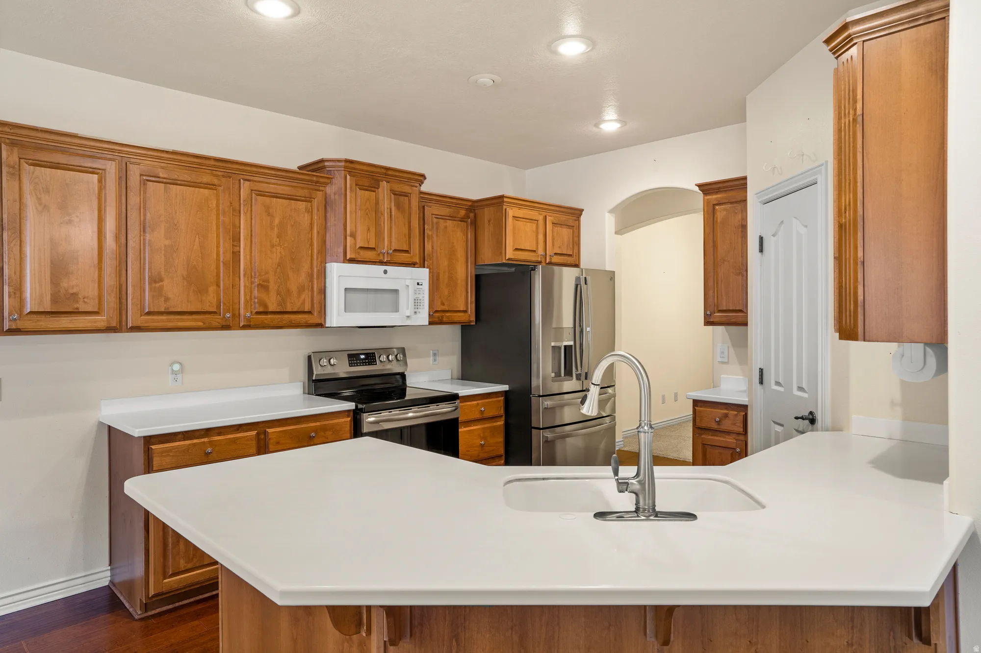 Kitchen with wood finish cabinets, stainless steel appliances, a peninsula, and light countertops