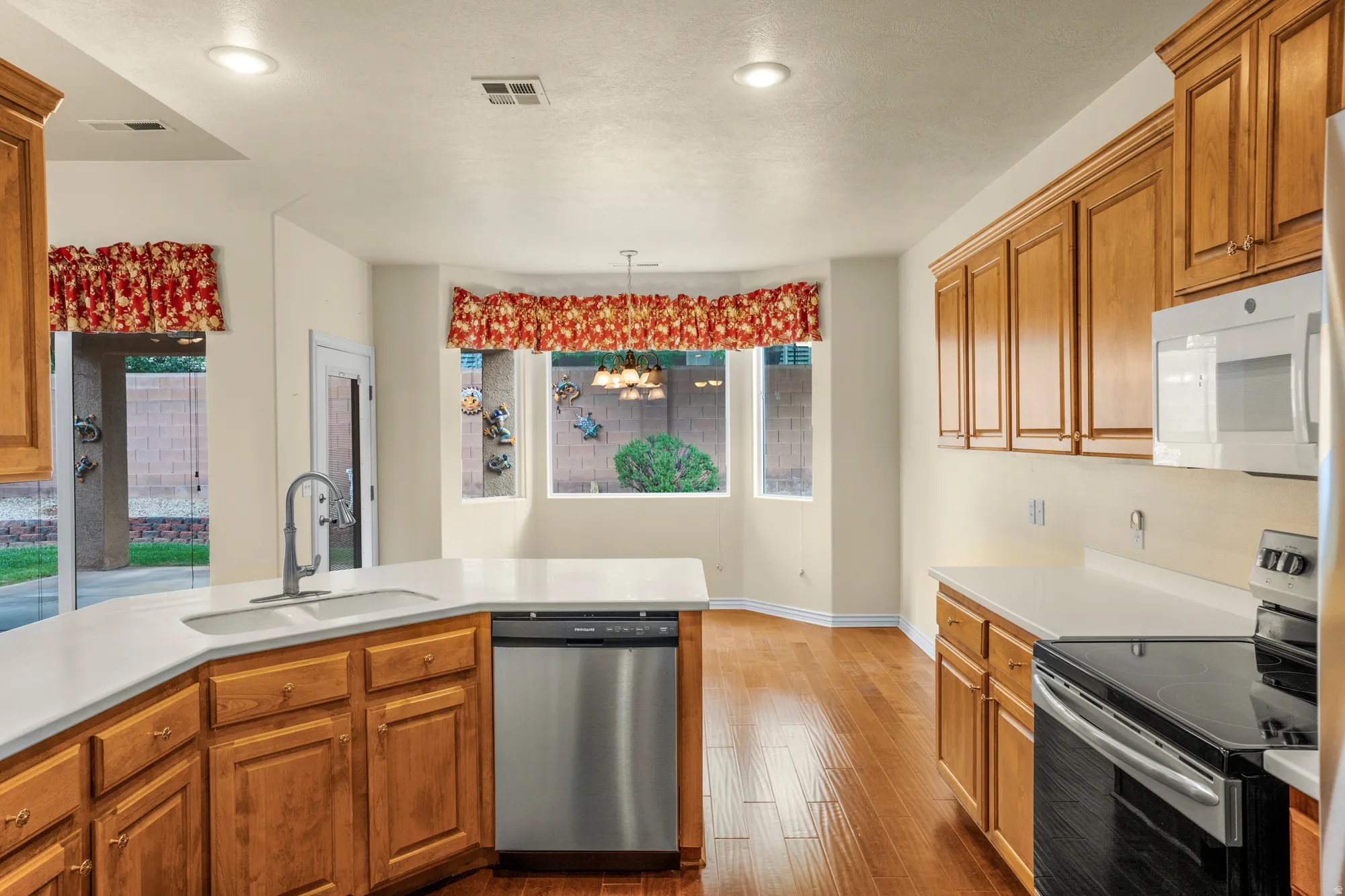 Kitchen featuring stainless steel appliances, wood finish cabinetry, dark wood-type flooring, and hanging light fixtures