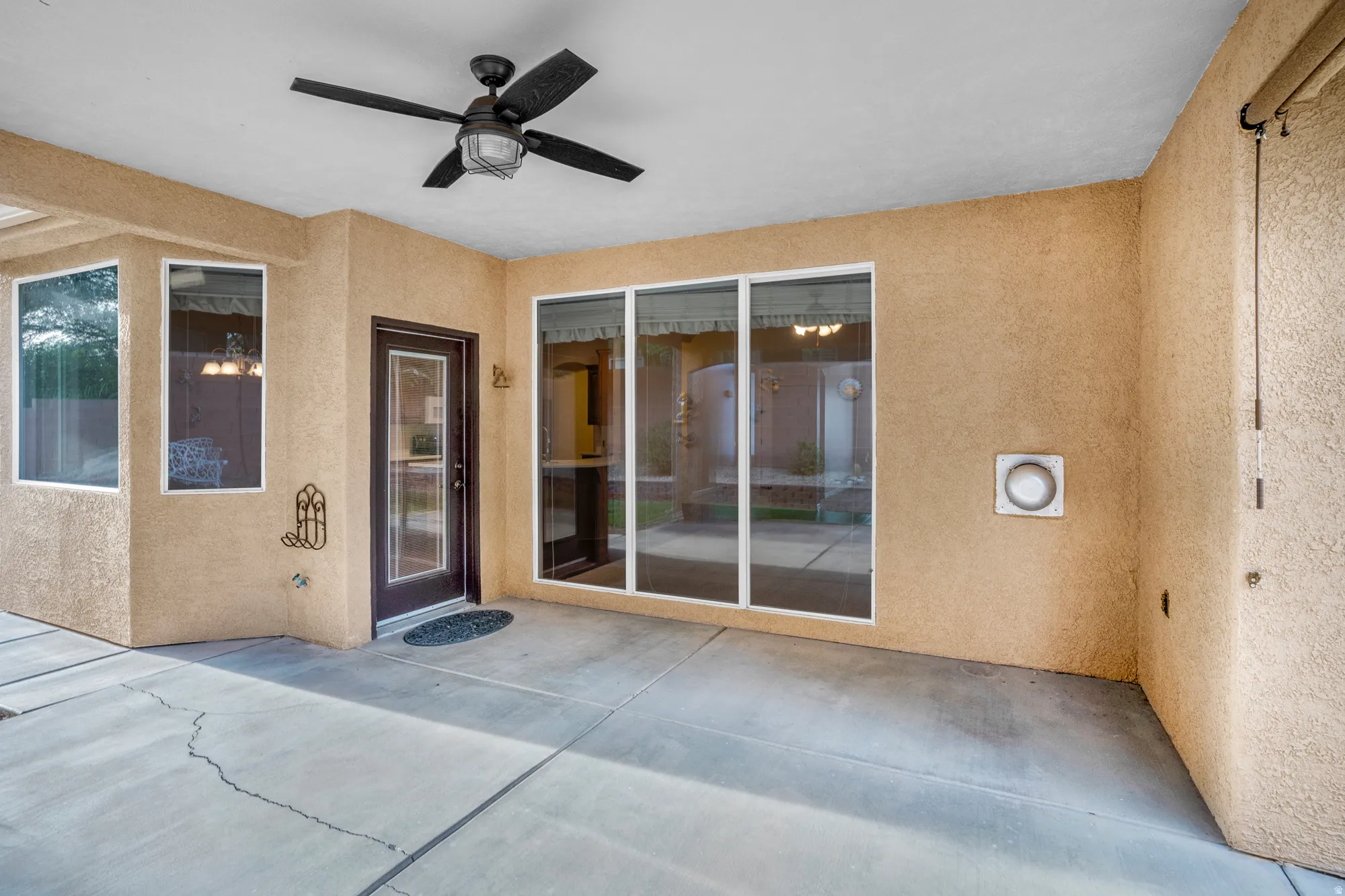 Entrance to property featuring ceiling fan, stucco siding, and a patio area