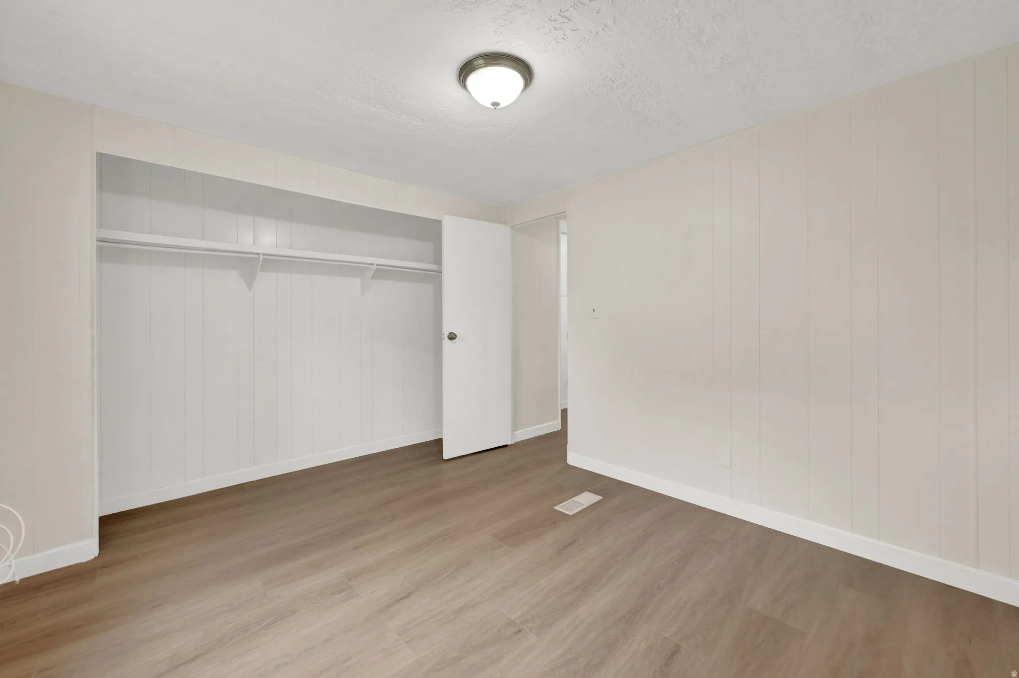 Unfurnished bedroom featuring light wood-style flooring, a closet, a textured ceiling, and wood walls