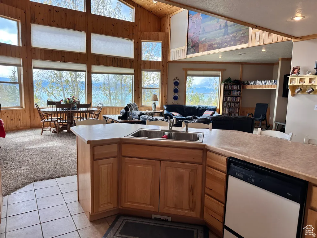 Kitchen featuring open floor plan, wood walls, light colored carpet, light countertops, and white dishwasher