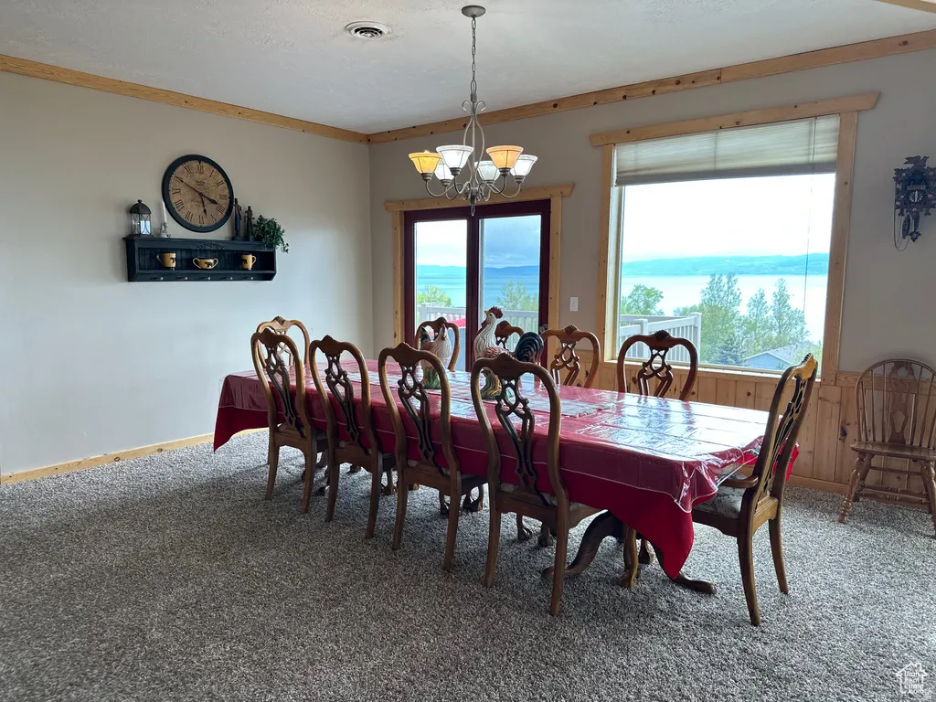 Carpeted dining room with a chandelier, wooden walls, and crown molding