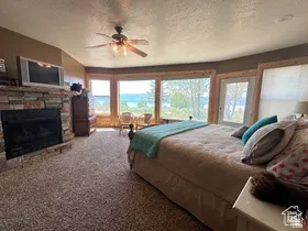 Bedroom with carpet, multiple windows, a stone fireplace, a ceiling fan, and a textured ceiling