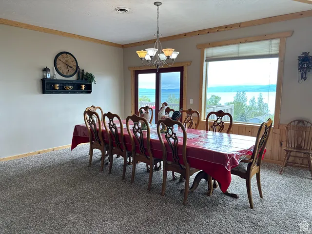 Carpeted dining room with a chandelier, wooden walls, and crown molding