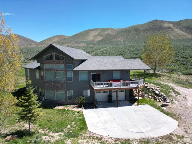 Rear view of property with an attached garage, a patio area, a deck with mountain view, driveway, and roof with shingles