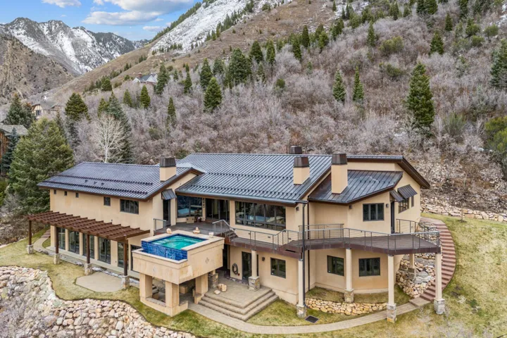 Back of house with a chimney, a standing seam roof, an outdoor hot tub, a deck with mountain view, and stucco siding