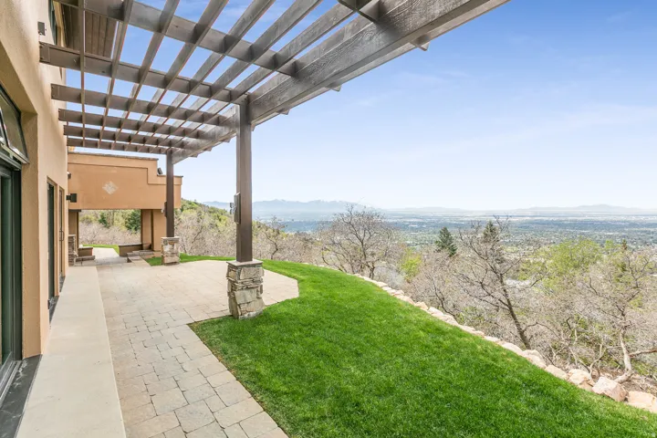 Expansive outdoor patio featuring paver stone flooring, a large wooden pergola, and stone-clad columns