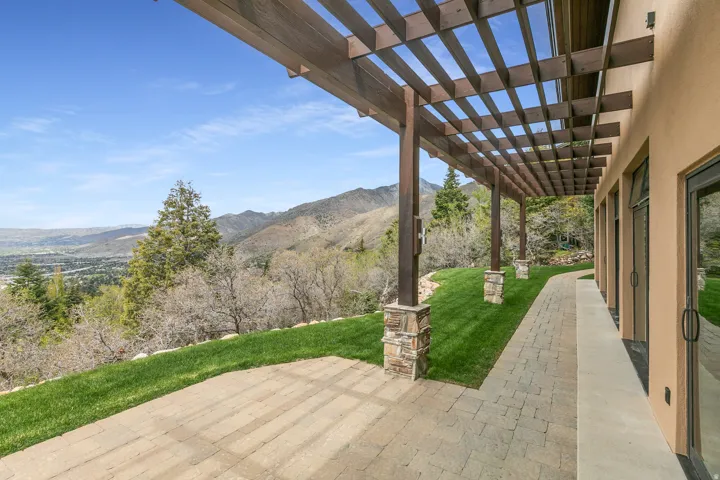 Expansive outdoor patio with a wooden pergola, stone-clad columns, and a paver walkway