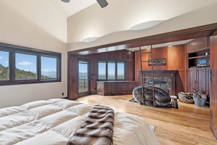 Primary suite featuring access to exterior, light hardwood flooring, a glass covered fireplace, vaulted ceiling, and a ceiling fan