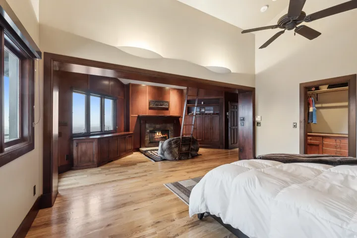Primary Bedroom with light hardwood floors, a lit fireplace, ceiling fan, and vaulted ceiling