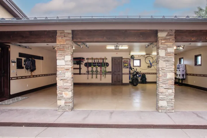 Three-car garage with stone-clad pillars, exposed wood beams, and a concrete floor