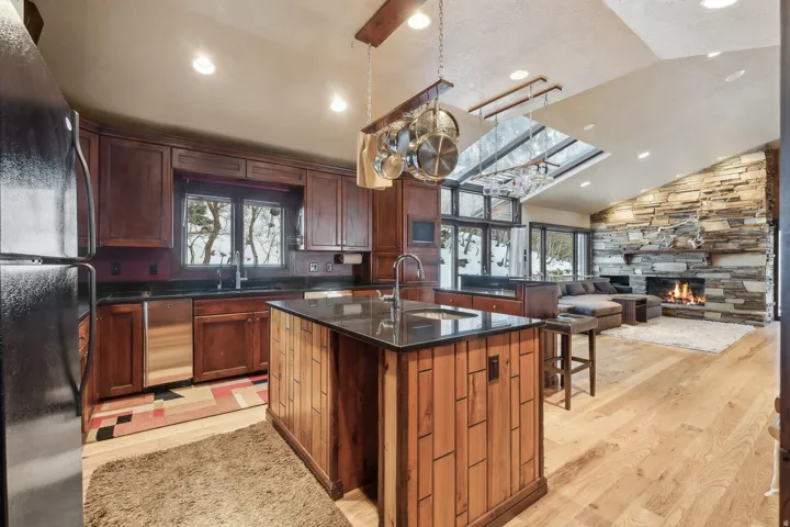 Kitchen with family room in background featuring a gas burning stone fireplace & custom Alder wood mantle.