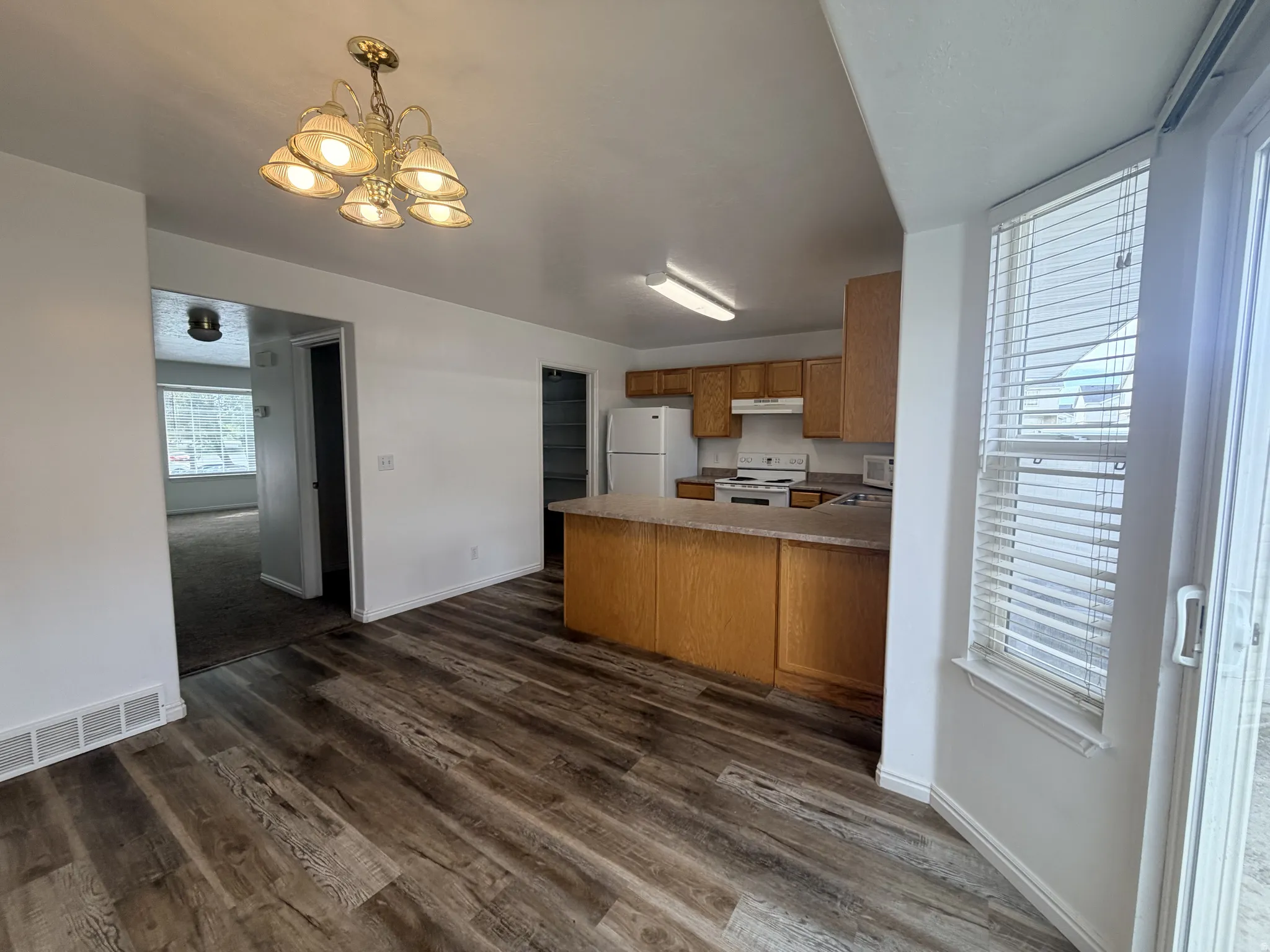 Kitchen featuring wood finish cabinets, suspended lighting, a peninsula, white appliances, and light countertops