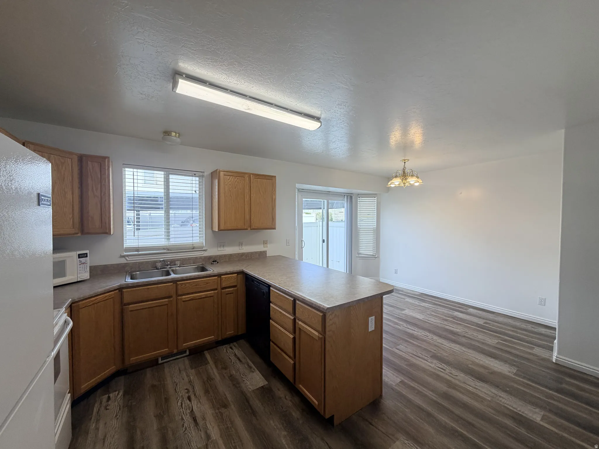 Kitchen featuring white appliances, a peninsula, wood finish cabinetry, a textured ceiling, and dark wood finished floors