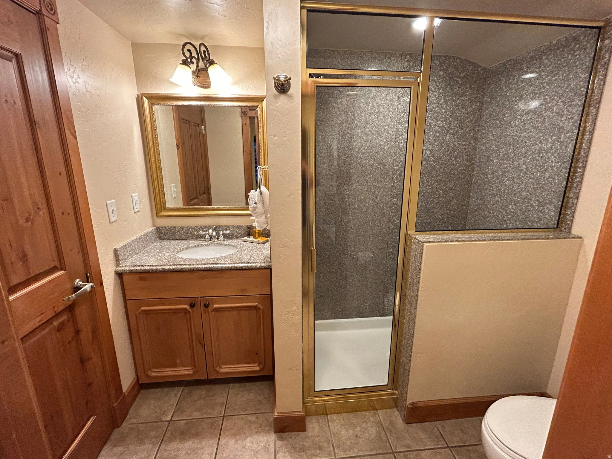 Bathroom with a textured wall, a shower stall, vanity, and light tile patterned floors