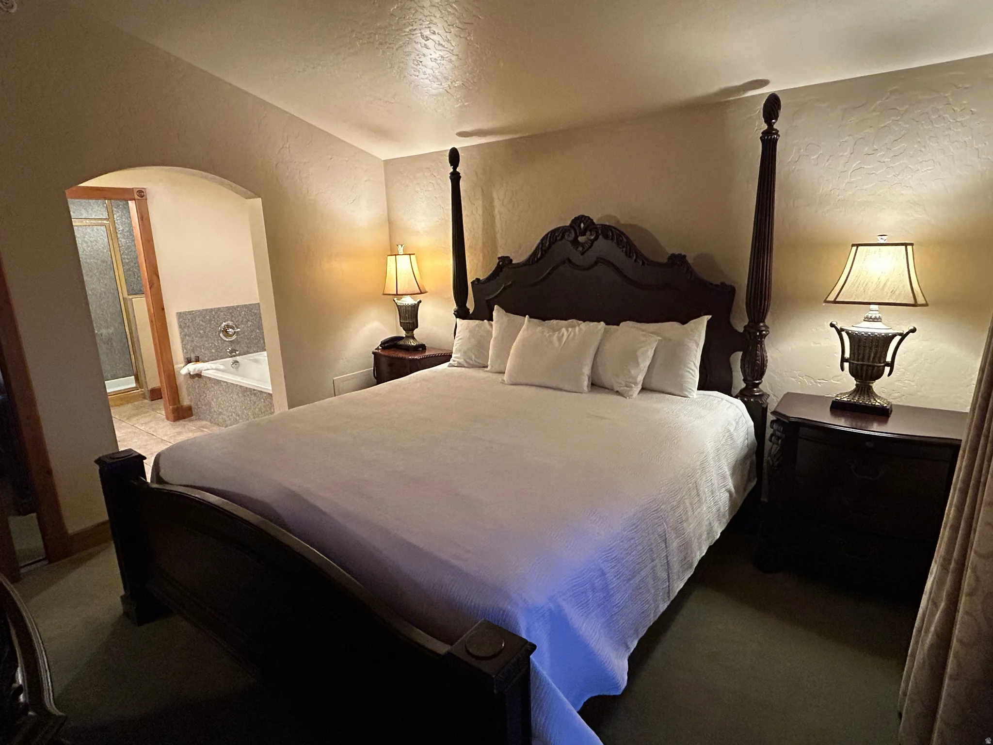 Bedroom with a textured wall, arched walkways, a textured ceiling, and connected bathroom