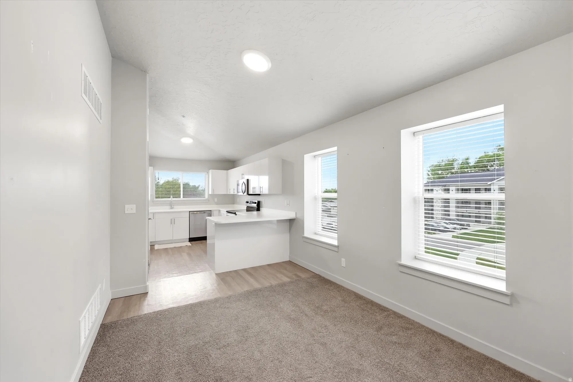 Kitchen featuring a peninsula, light countertops, white cabinetry, light colored carpet, and stainless steel appliances