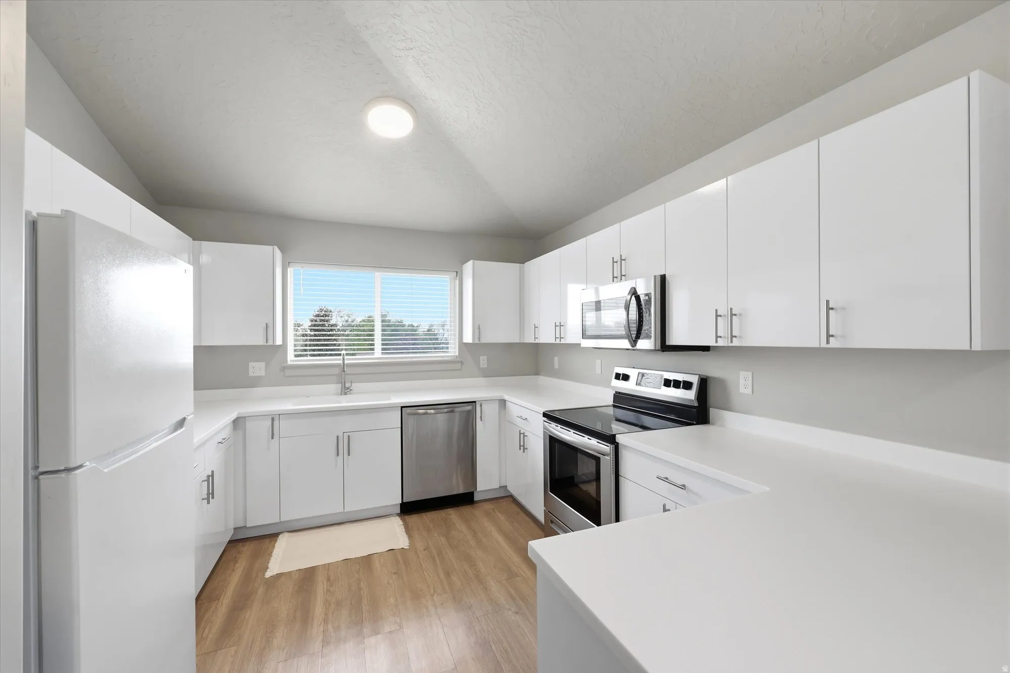 Kitchen featuring stainless steel appliances, light countertops, white cabinetry, and light wood-style flooring