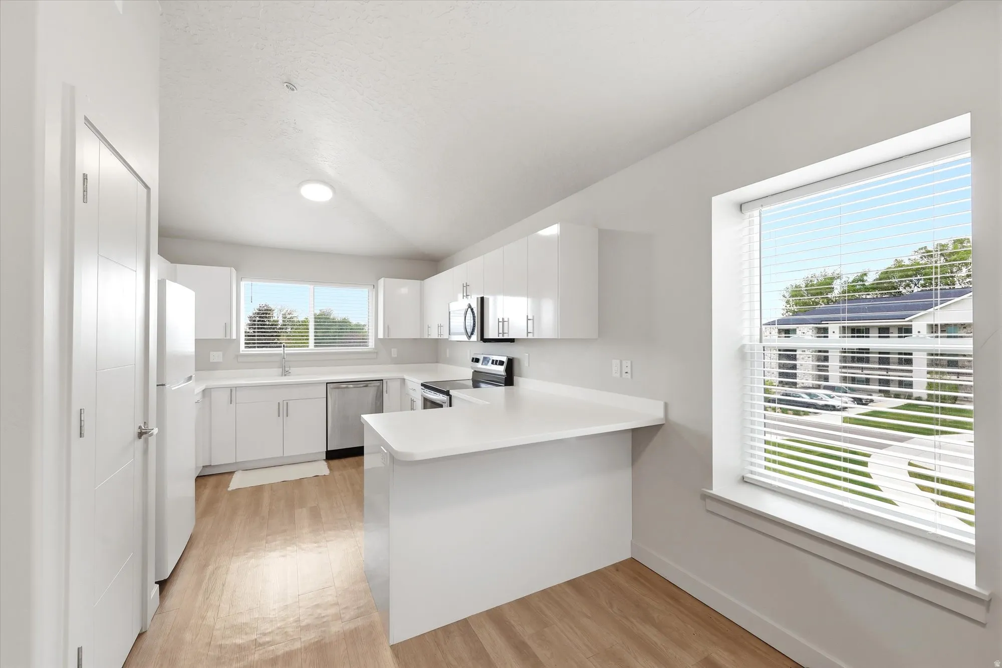 Kitchen with a peninsula, light countertops, white cabinets, vaulted ceiling, and stainless steel appliances
