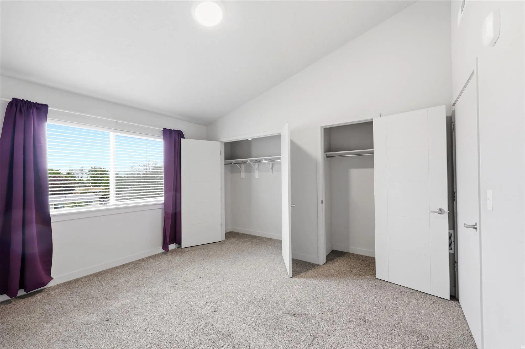 Unfurnished bedroom featuring two closets, lofted ceiling, and light carpet