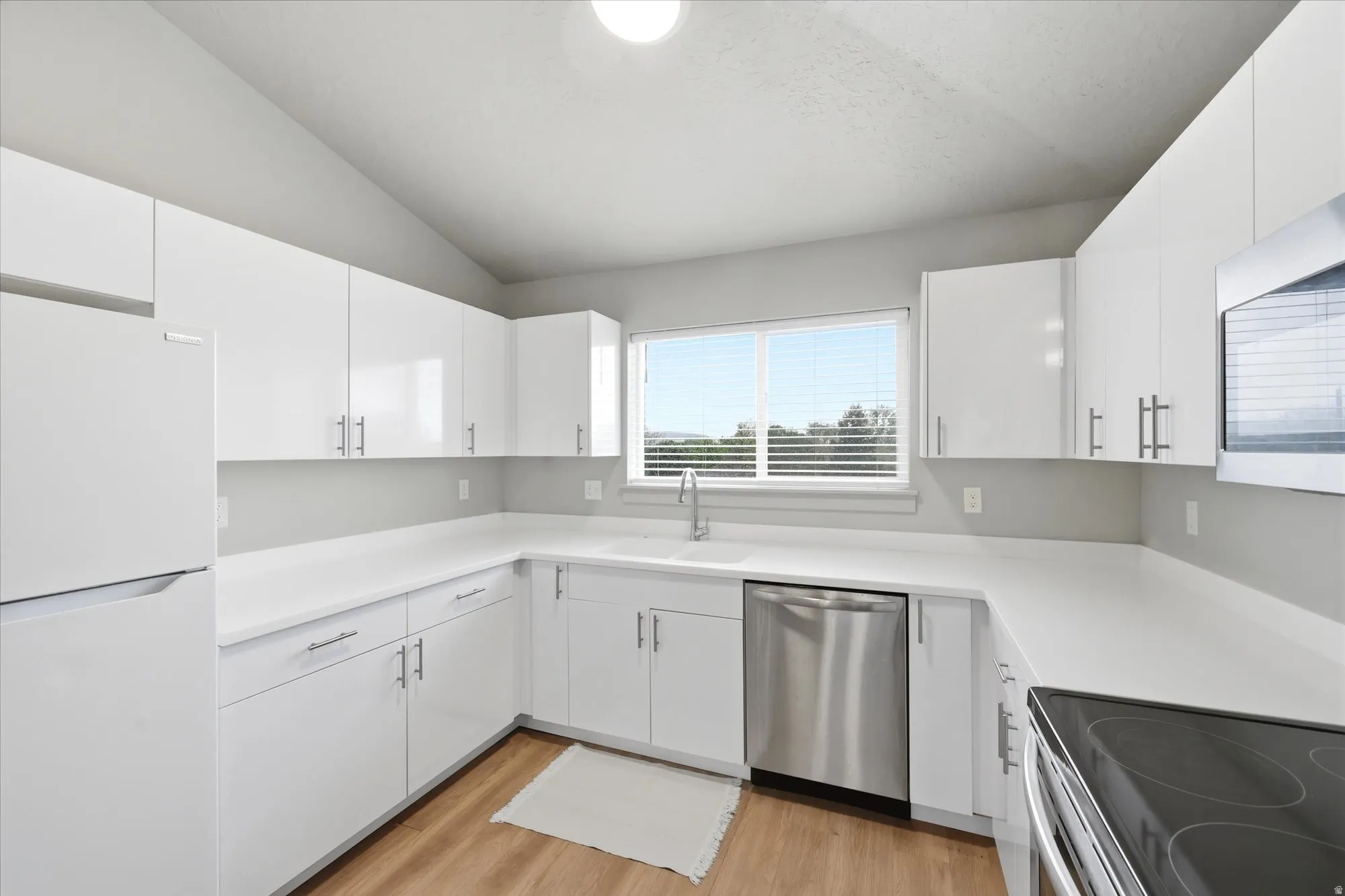Kitchen with stainless steel appliances, white cabinets, vaulted ceiling, and light wood-style flooring