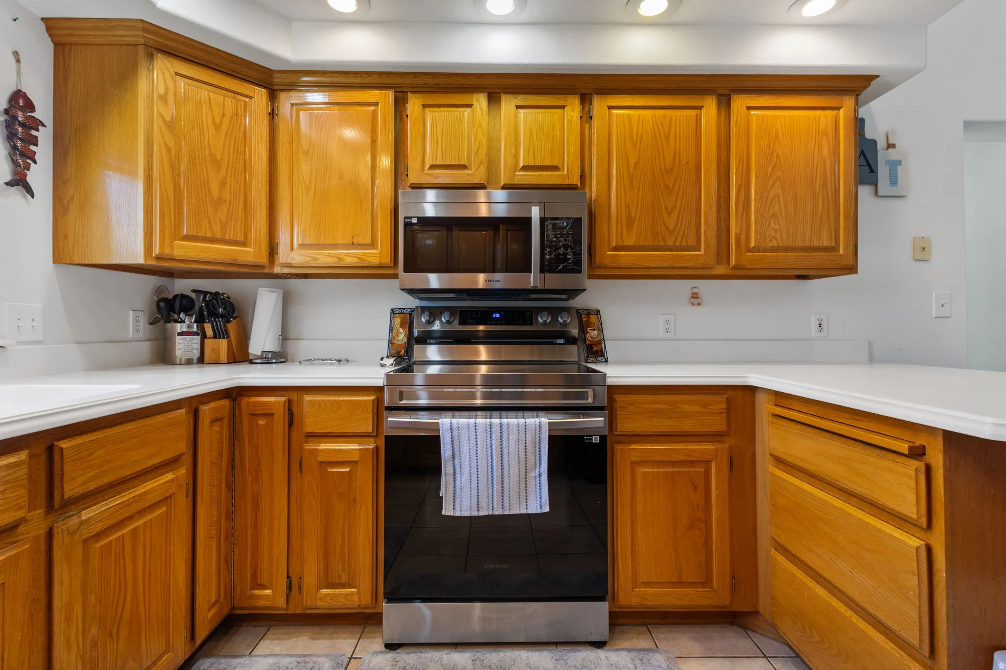 Kitchen with stainless steel appliances, wood finish cabinetry, light countertops, light tile patterned flooring, and recessed lighting
