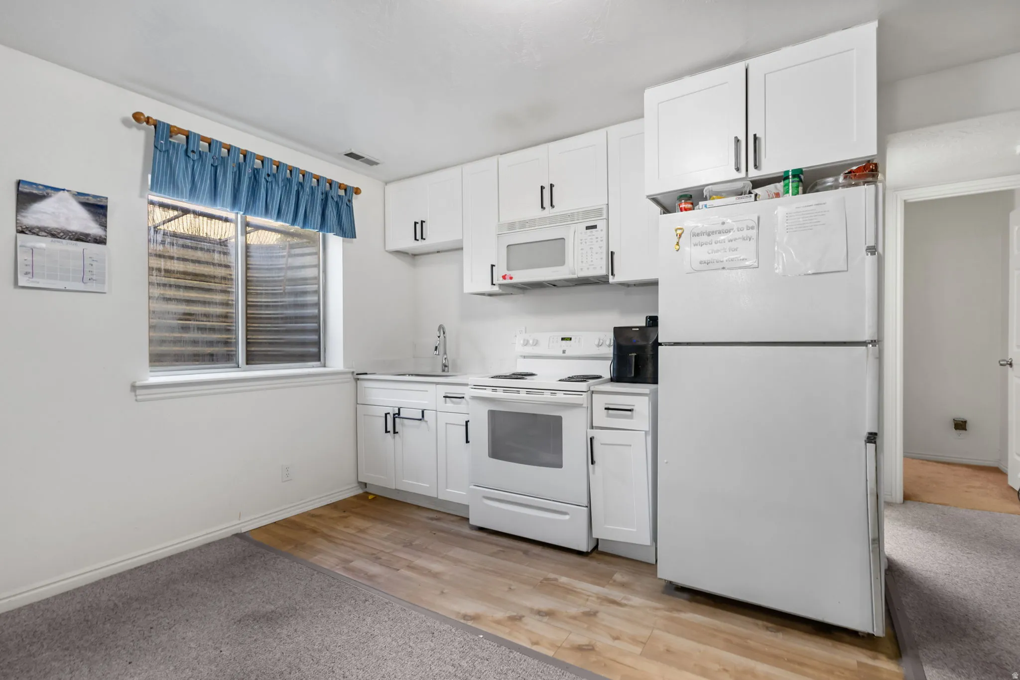 Kitchen with white appliances, light wood-style floors, white cabinetry, and light countertops