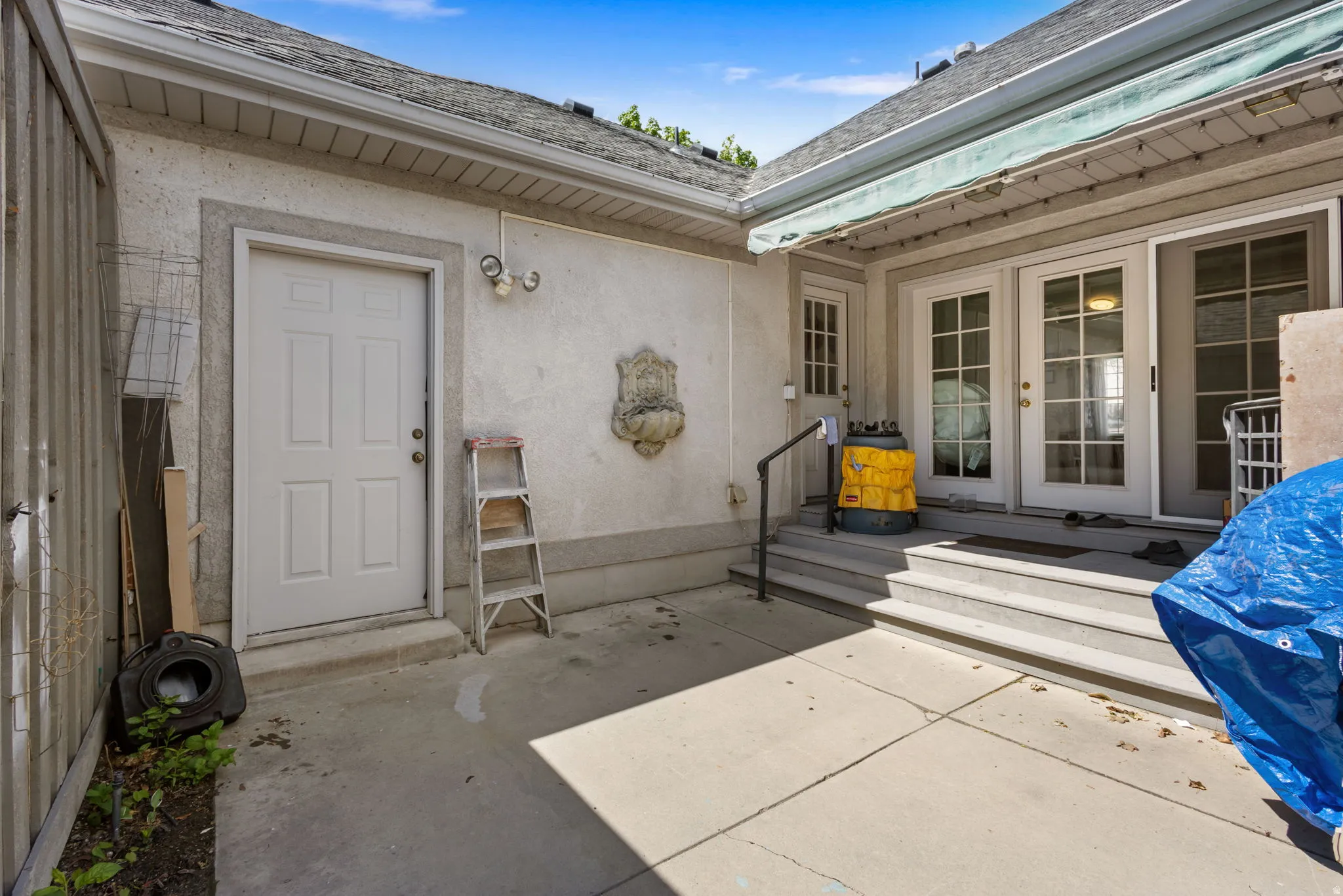 View of exterior entry with stucco siding, a shingled roof, french doors, and a patio area