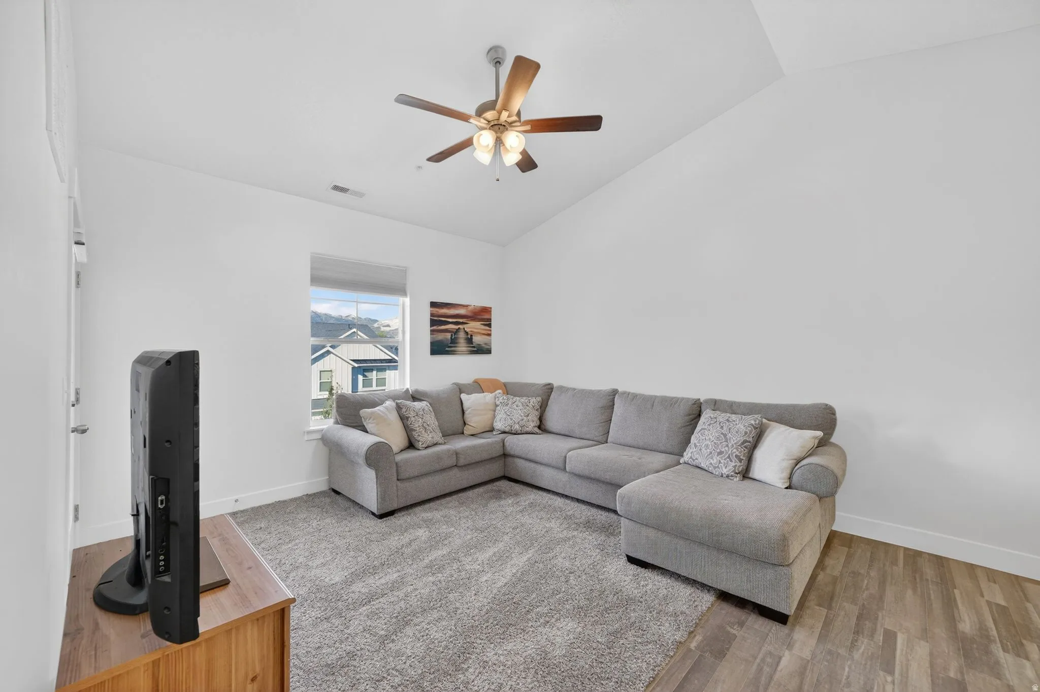 Living area featuring vaulted ceiling, light wood-style floors, and a ceiling fan