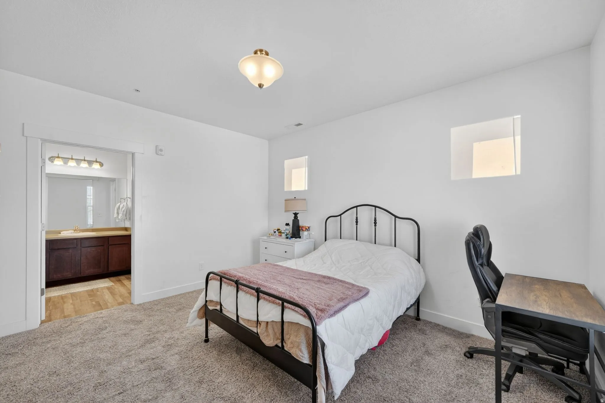 Bedroom featuring light carpet, a desk, and ensuite bathroom
