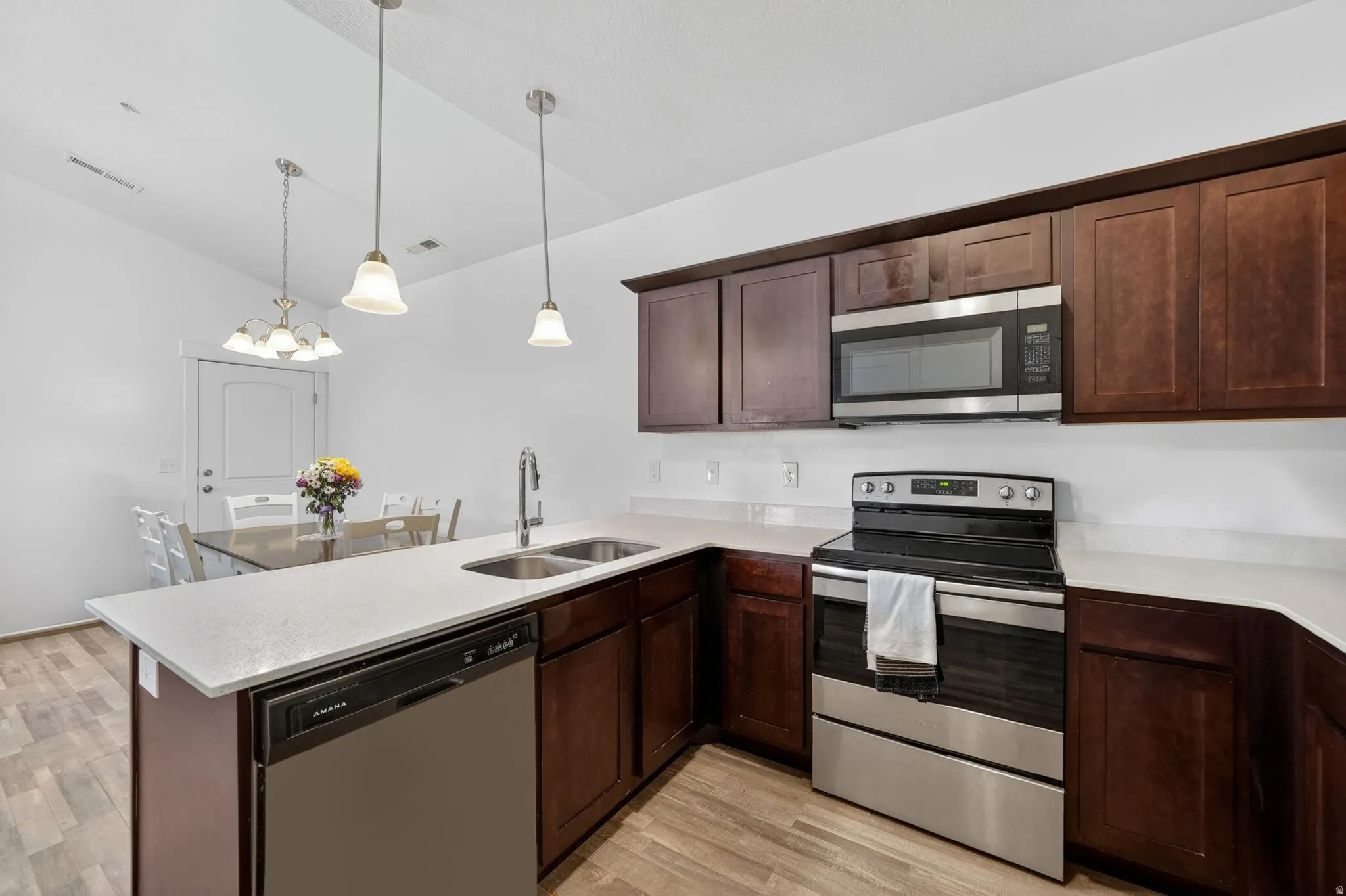 Kitchen with stainless steel appliances, dark wood finish cabinetry, a peninsula, light wood-style flooring, and vaulted ceiling