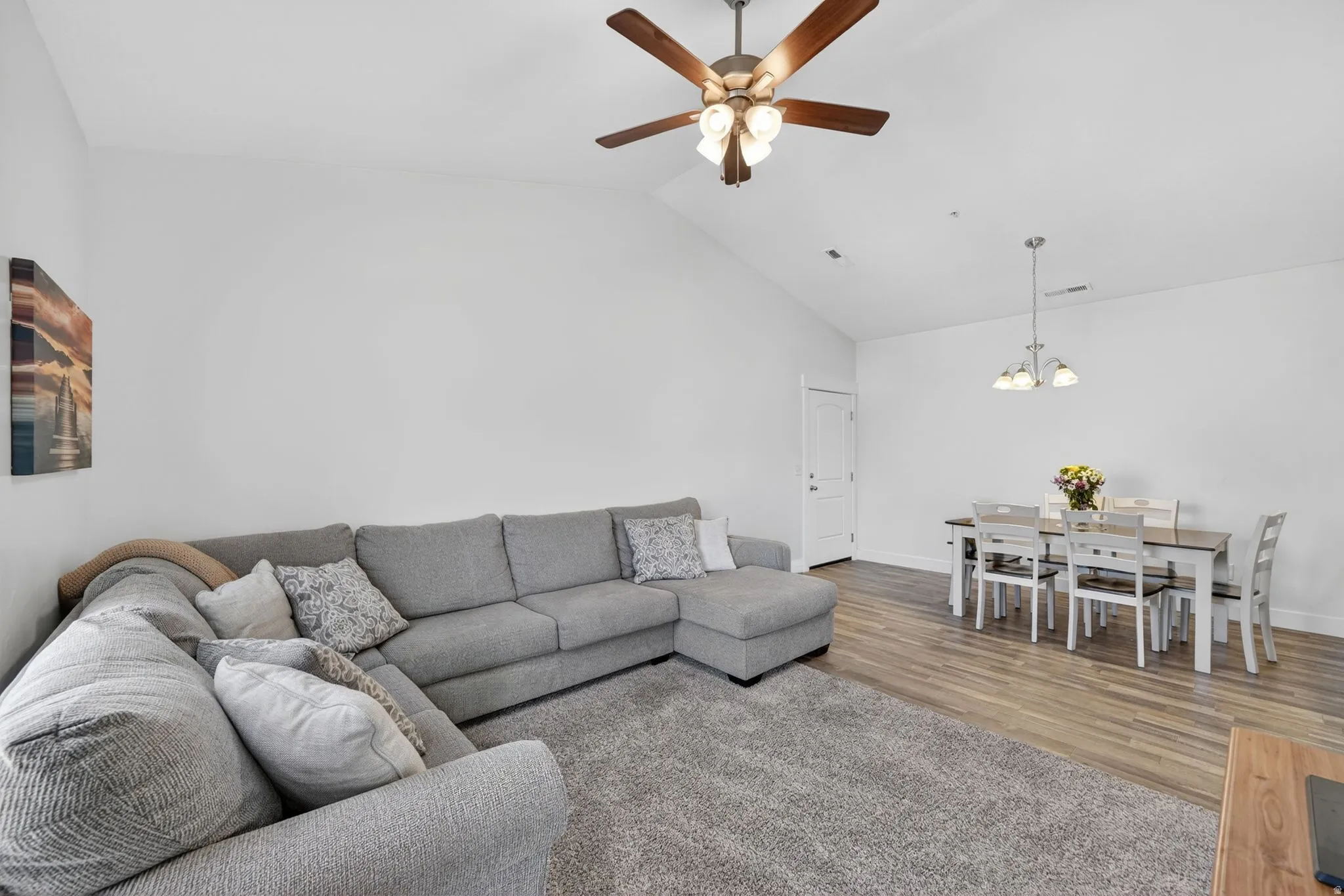 Living area with lofted ceiling, ceiling fan, wood finished floors, and a chandelier
