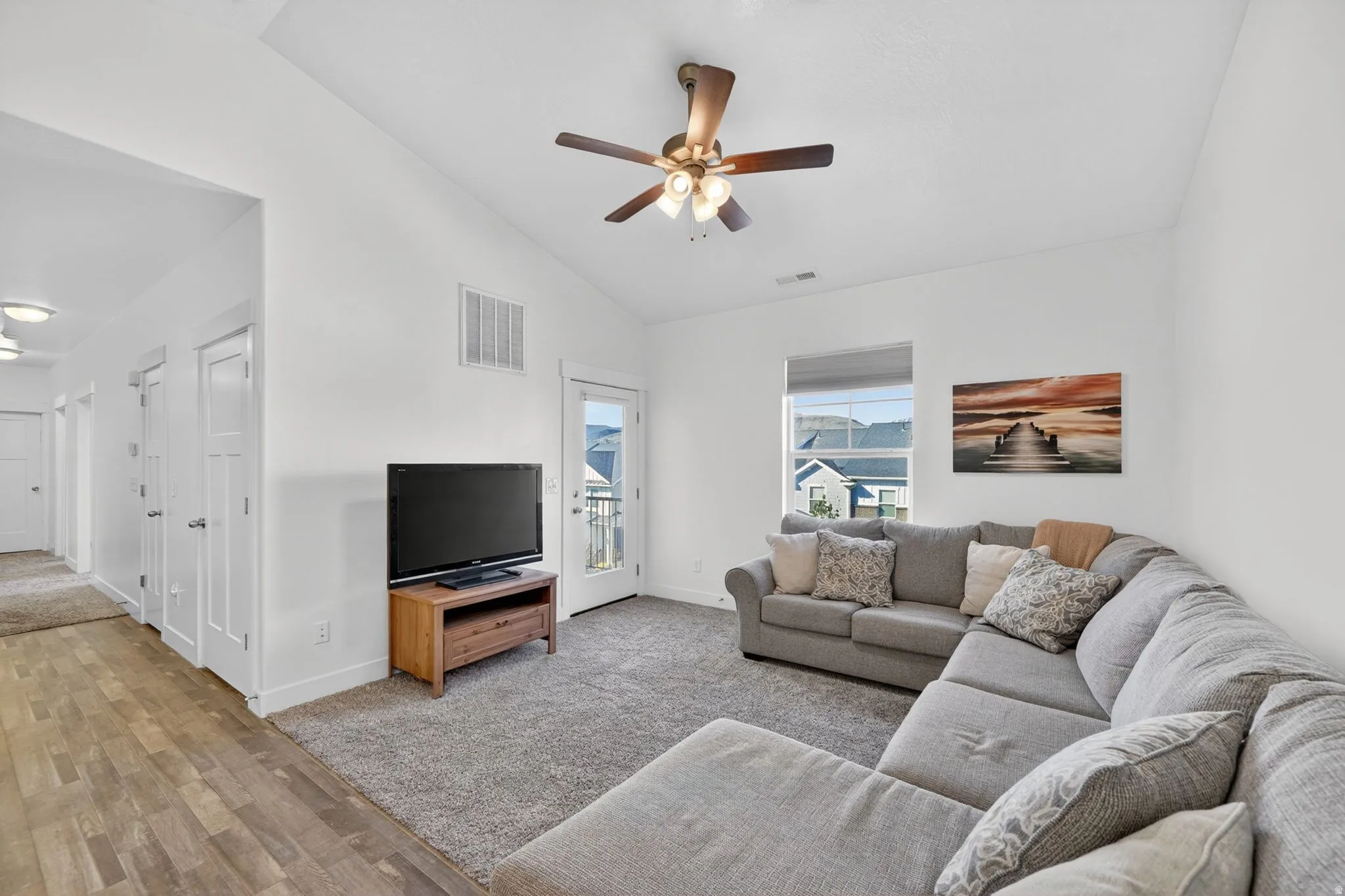 Living area with vaulted ceiling, ceiling fan, light wood-type flooring, and light carpet