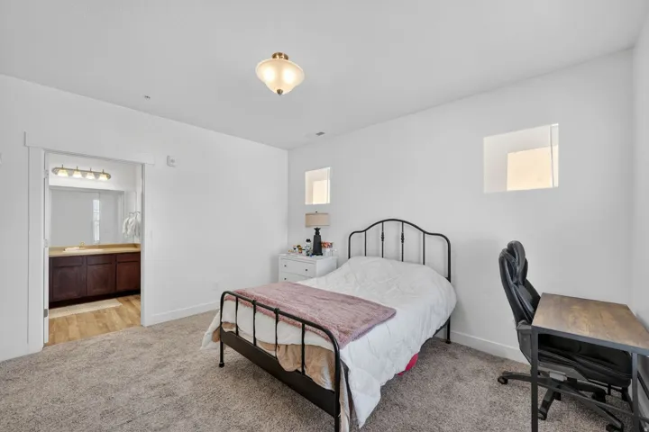 Bedroom featuring light carpet, a desk, and ensuite bathroom