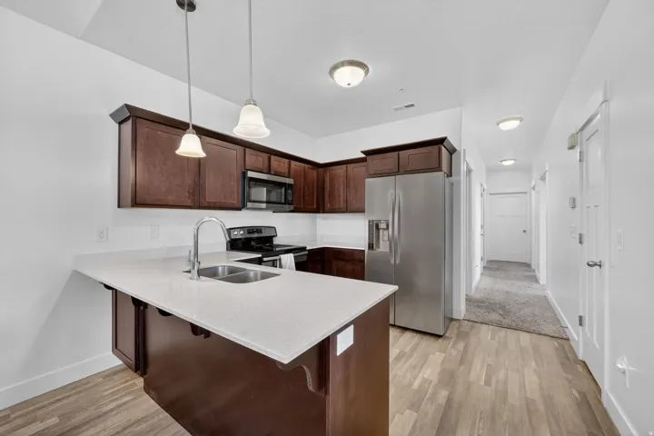 Kitchen featuring dark wood finish cabinets, a breakfast bar area, a peninsula, stainless steel appliances, and light wood finished floors