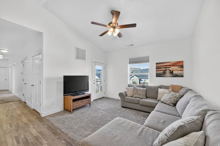 Living area with vaulted ceiling, ceiling fan, light wood-type flooring, and light carpet
