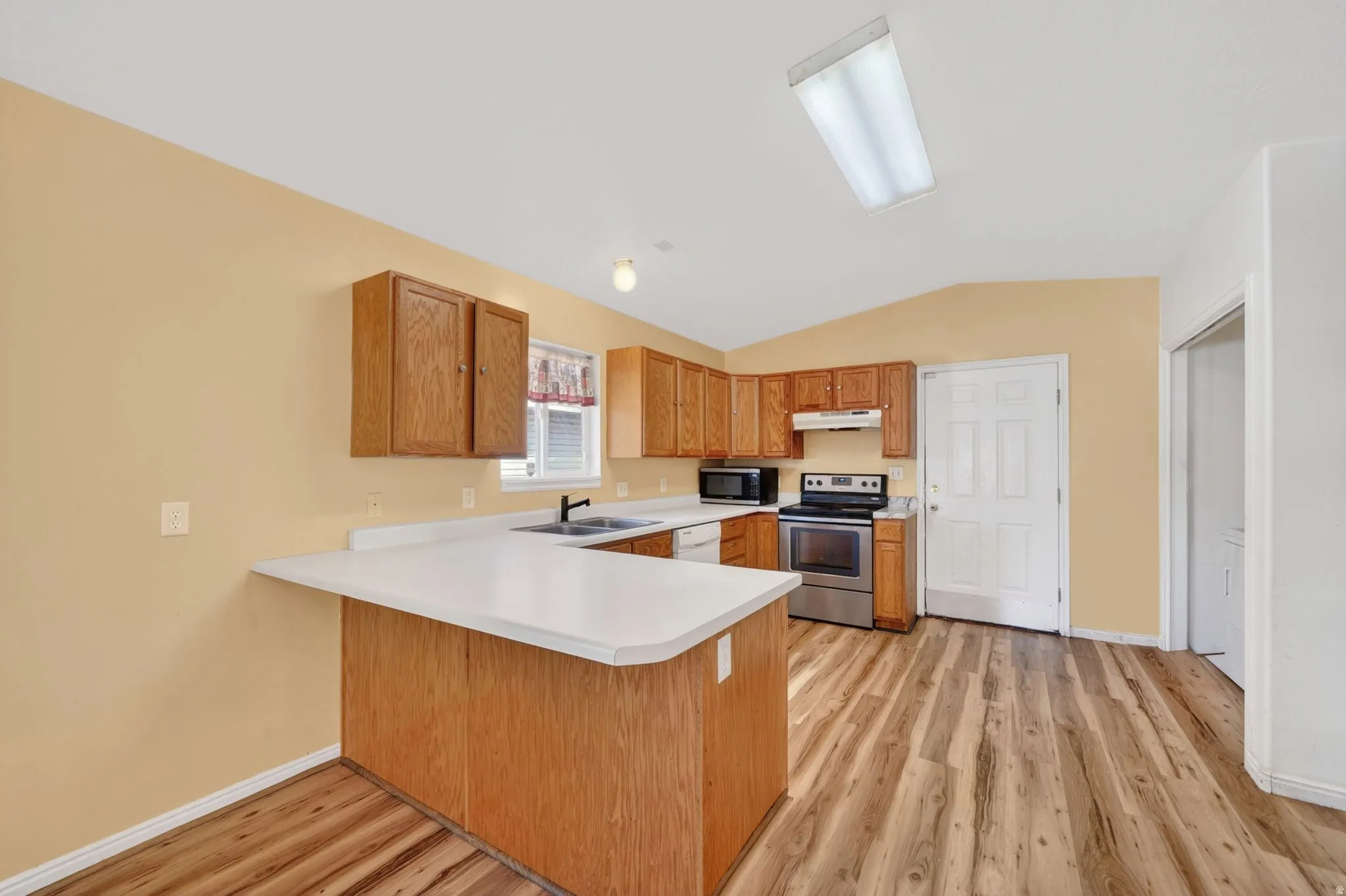 Kitchen featuring a peninsula, light countertops, stainless steel electric stove, light wood-style floors, and vaulted ceiling