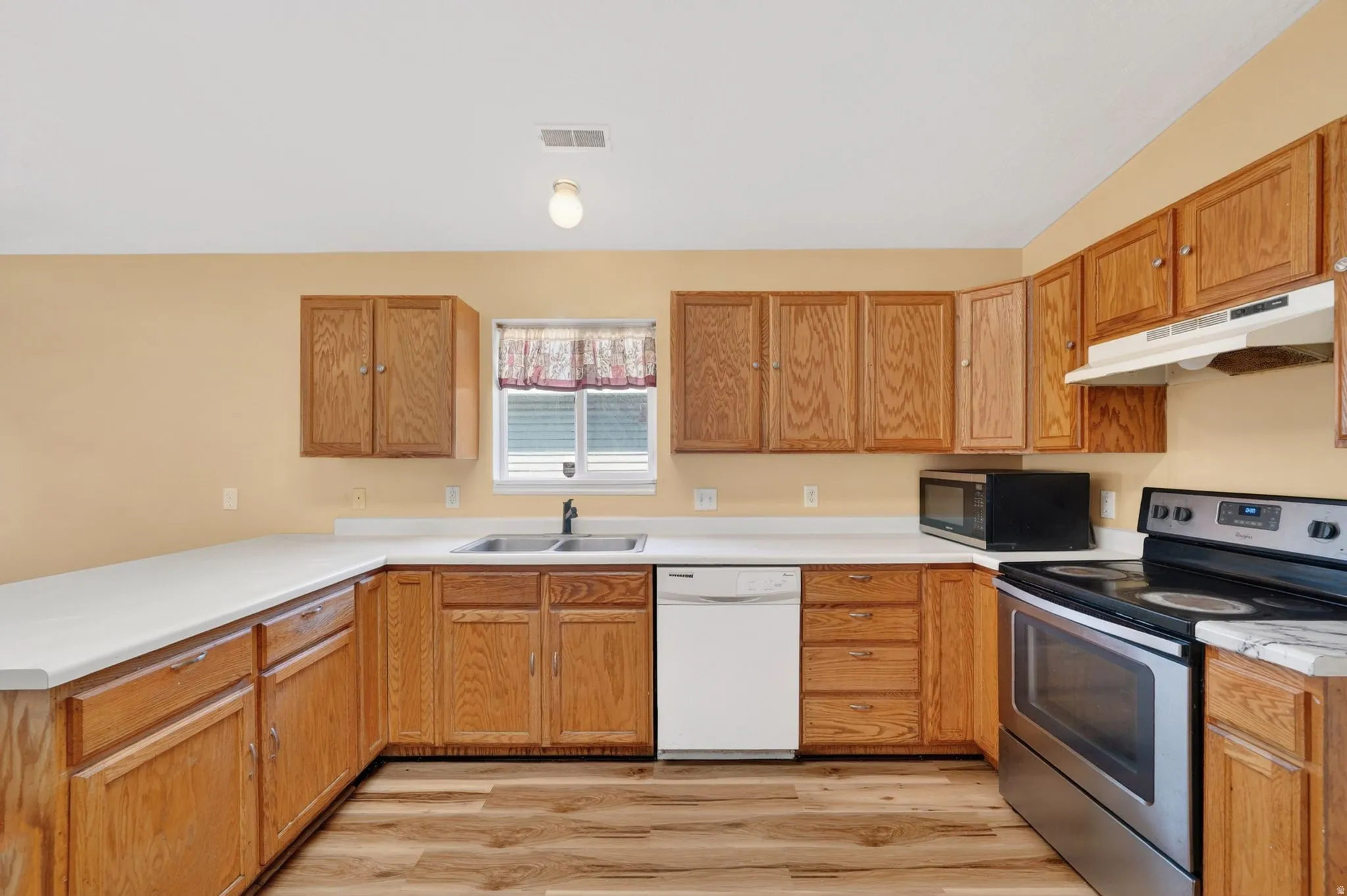 Kitchen with stainless steel electric range oven, light countertops, a peninsula, dishwasher, and wood finish cabinetry
