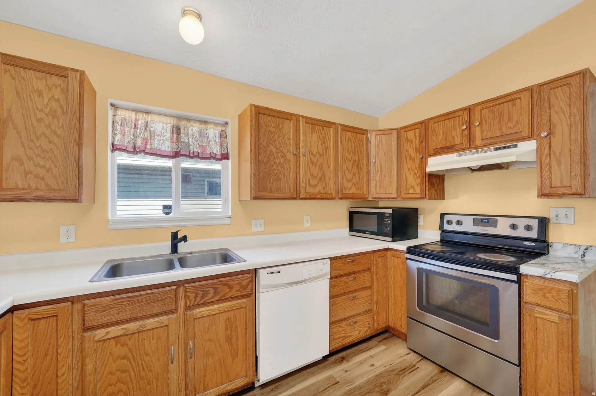 Kitchen featuring stainless steel electric range, light countertops, dishwasher, black microwave, and light wood-style flooring