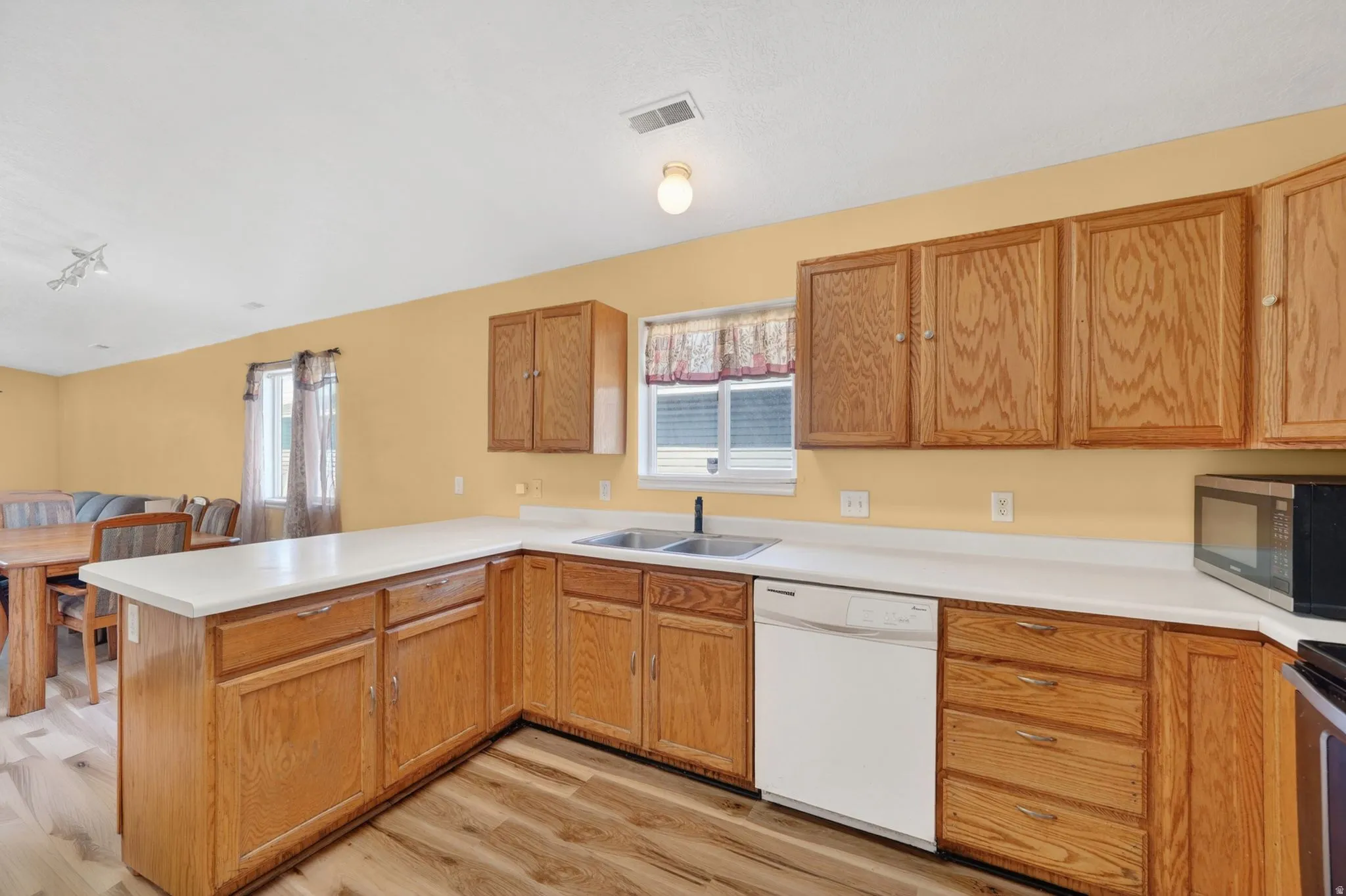 Kitchen with a peninsula, light countertops, white dishwasher, light wood-type flooring, and stainless steel microwave